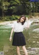 A woman in a white shirt and black skirt standing in a river.