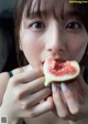 A woman eating a fig in front of her face.