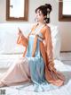 A woman in a blue and orange dress sitting on a bed.
