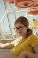 A woman wearing glasses sitting in front of a ferris wheel.