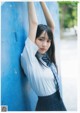 A young woman leaning against a blue wall.