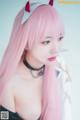 A woman with long pink hair wearing a devil horns headband.