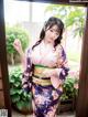 A woman in a kimono standing in front of a window.