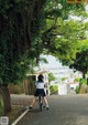 A woman riding a bike down a street next to a tree.